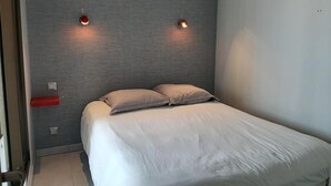 Une chambre avec un lit simple, des murs gris à texture et deux lampes fixées au mur.