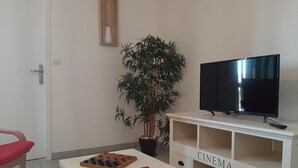 Un salon comprenant un téléviseur, un jeu d’échecs, un fauteuil rouge, une plante en pot et un meuble blanc sur lequel est inscrit le mot « CINÉMA ».