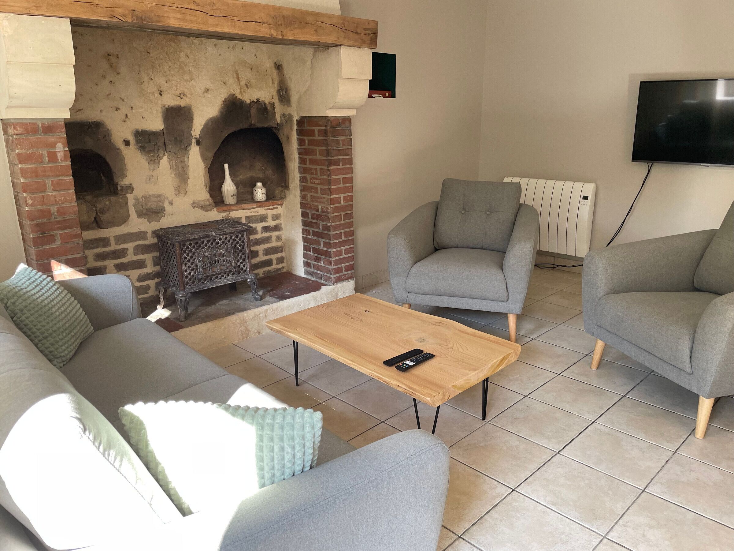 Ein Wohnzimmer mit Kamin, grauen Sofas, einem Holztisch und einem an der Wand befestigten Fernseher.