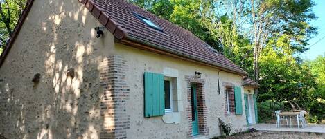 A rustic house with a tiled roof, brick walls, and green shutters.