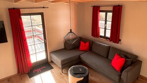 Un salon moderne avec un canapé d’angle gris, des coussins rouges, un luminaire suspendu et un plancher en bois.