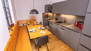 Une cuisine moderne avec une table à manger en bois, des meubles de rangement gris et un luminaire suspendu noir.