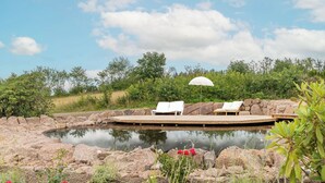 Un espace piscine extérieur paisible, avec des chaises longues et une terrasse en bois, entouré d’une végétation luxuriante et surplombé d’un ciel dégagé.
