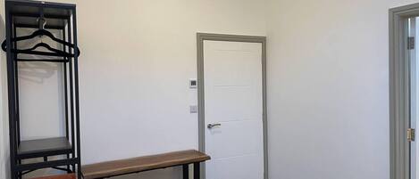 Ett sovrum med en säng, ett skrivbord, en hängande garderob och en dörr.