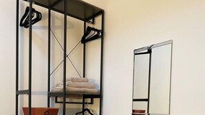 A room with a black metal shelving unit containing folded towels and baskets, a wooden table with a round stool, and a mirror on the wall. - Smithy Bungalow, Free Private Parking (Buxton)
