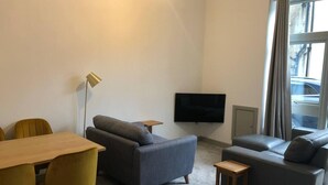 A modern living room with a sofa, a small table, a TV, and a window with curtains. - Smithy Bungalow, Free Private Parking (Buxton)