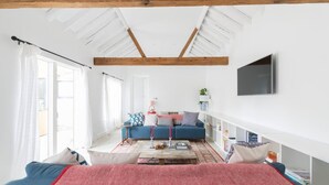 Ein geräumiges Zimmer mit hoher Decke, einem großen Bett, einem blauen Sofa und einem Bücherregal.