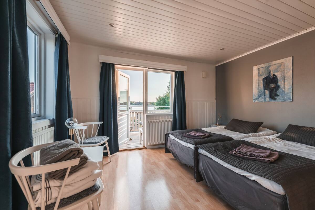 A hotel room with two beds, a chair, a table, and a painting on the wall.