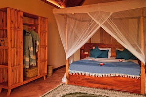 A wooden four-poster bed with a canopy, a wardrobe with hanging clothes, and a woven basket on the floor. - Kidoti Bay (Kidoti)