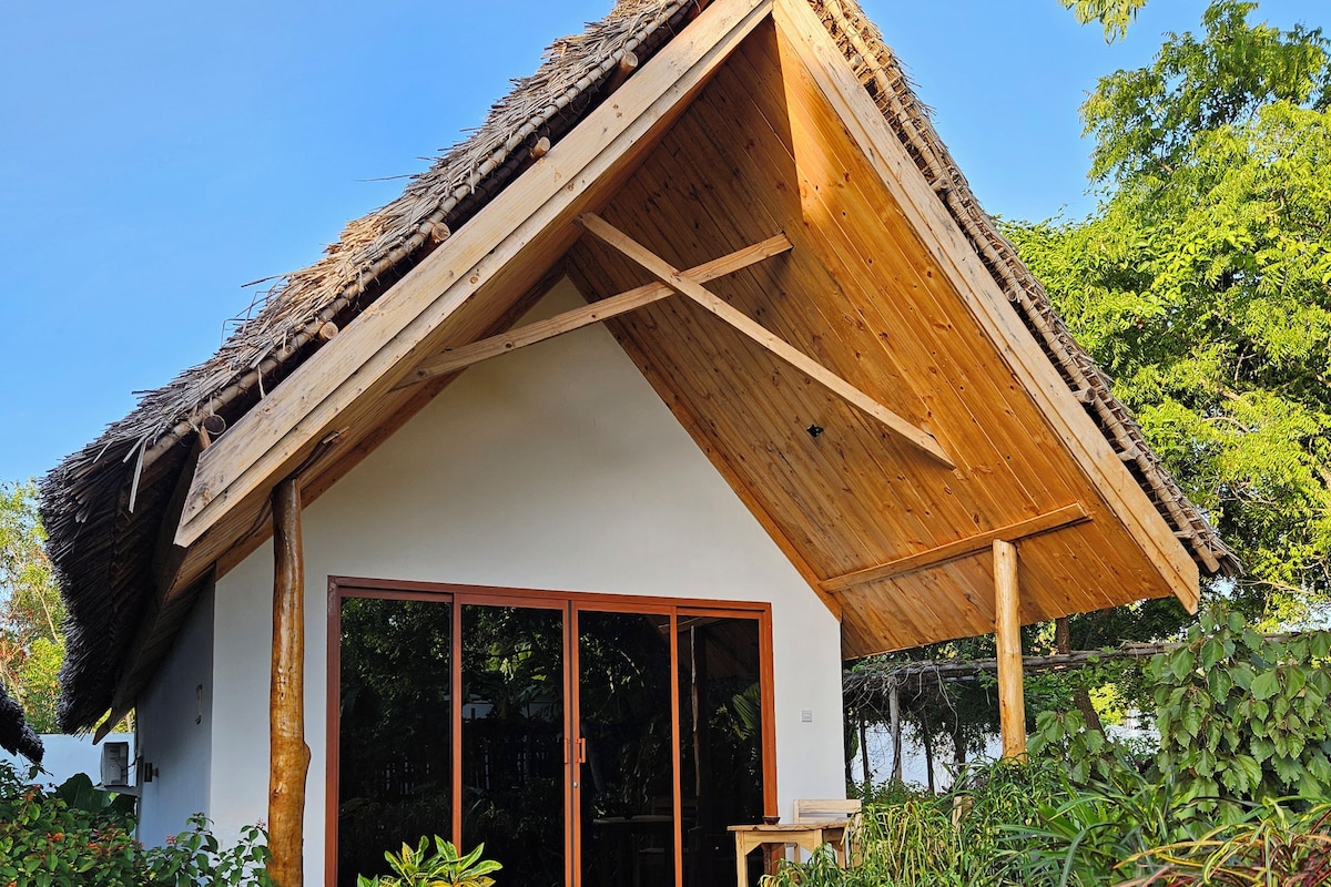 A house with a thatched roof, large windows, and a gravel pathway leading to the entrance.