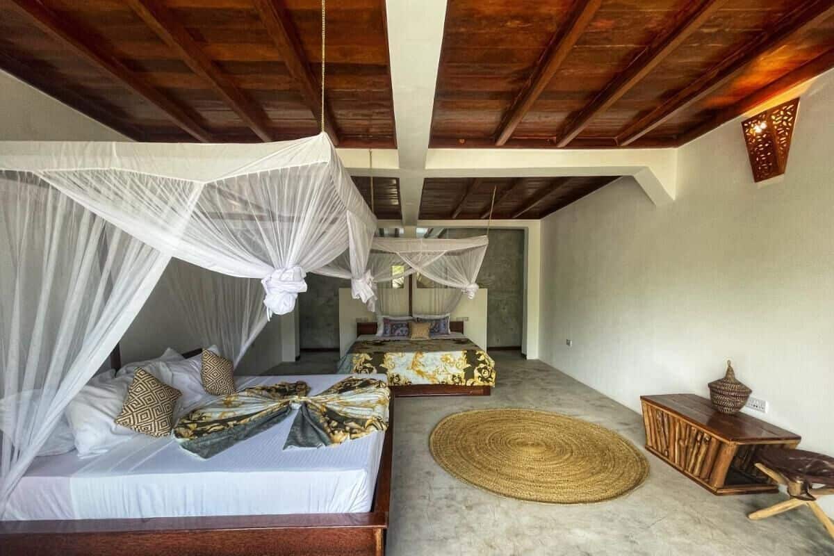 A bedroom with a bed under a canopy, a second bed, a woven mat, and a wooden side table.