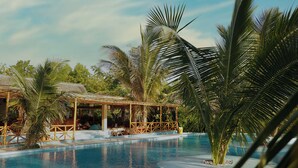 A swimming pool with a wooden deck and lounge chairs, surrounded by palm trees and a covered seating area. - Kidoti Bay (Kidoti)