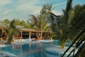 A swimming pool with a wooden deck and lounge chairs, surrounded by palm trees and a covered seating area. - Kidoti Bay (Kidoti)