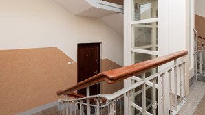 Una escalera con barandales blancos y un pasamanos de madera, que conduce a una habitación con un amplio ventanal y una puerta.