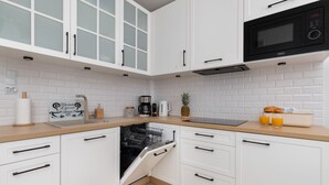 Una cocina moderna con armarios blancos, microondas, cafetera y lavavajillas.