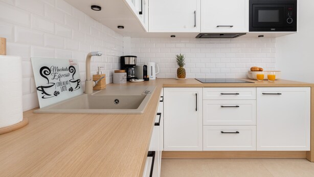 Una cocina moderna con armarios blancos, un lavamanos de acero inoxidable, una cafetera y un microondas.
