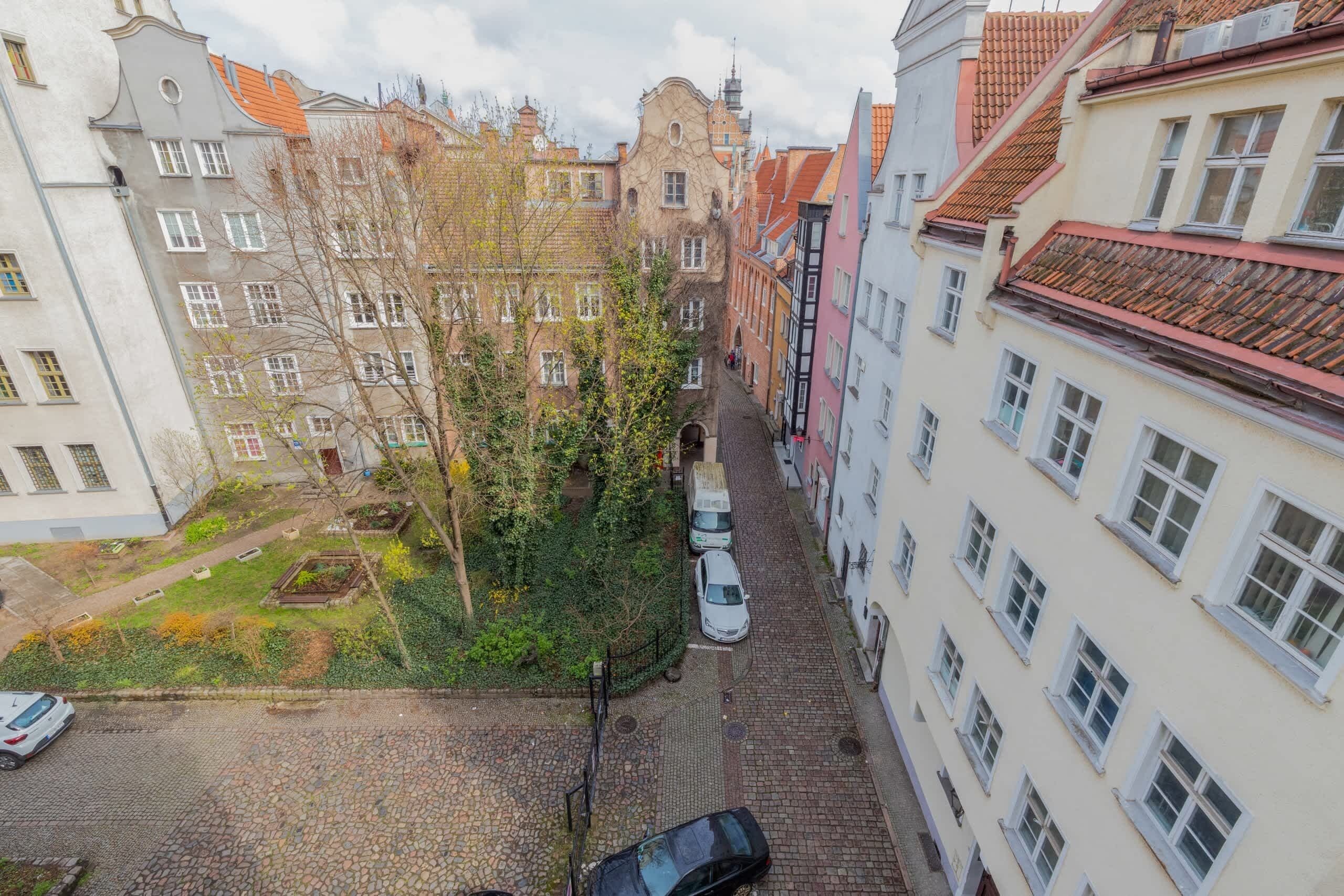 A narrow cobblestone street flanked by multi-story buildings with traditional European architecture, including visible windows and balconies.