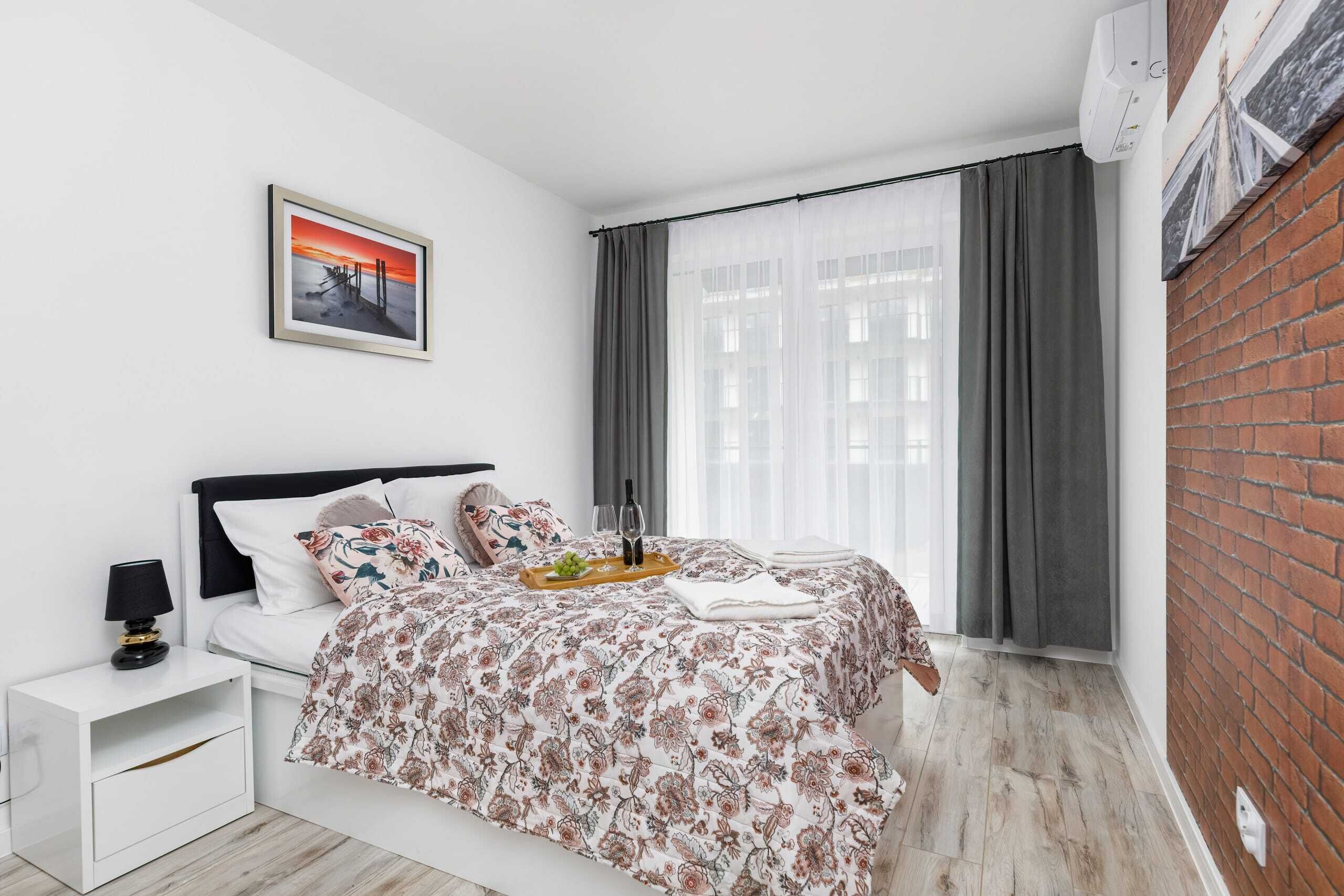 A modern bedroom with a bed, a nightstand, a framed picture, and a window with curtains.
