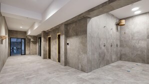 Un couloir moderne avec un sol et des murs carrelés de couleur grise, agrémenté d’une porte en bois et d’un petit seau en bois fixé au mur.