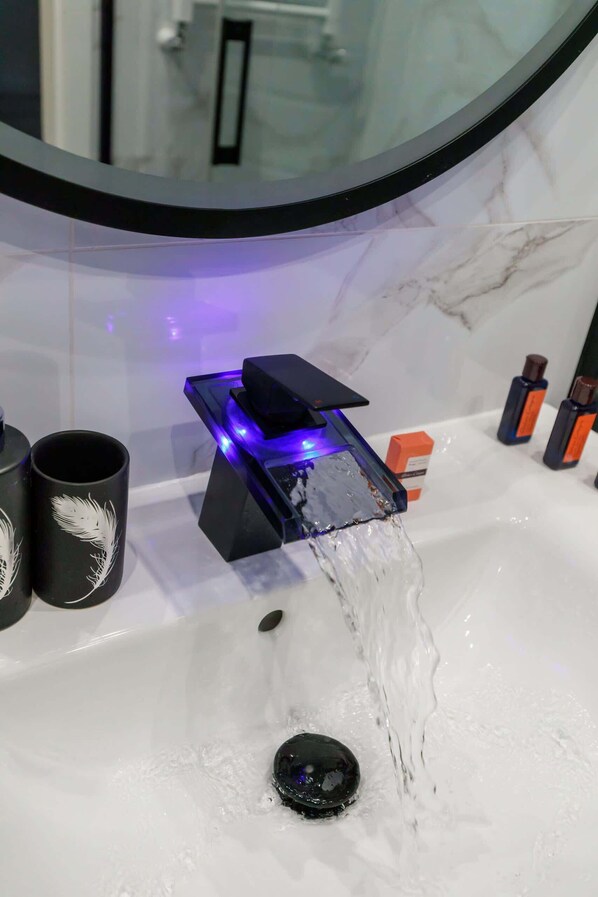 A bathroom with a modern sink, a mirror, and a blue-lit faucet.