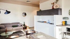 Una sala de estar moderna con un sofá gris, una mesa de centro de cristal y una zona de comedor con una mesa y sillas blancas.