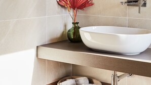 Un baño con un espejo grande, un lavamanos blanco y un florero con flores rojas.