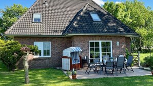 A house with a tiled roof, a brick exterior, a covered patio with outdoor furniture, and a small garden area.