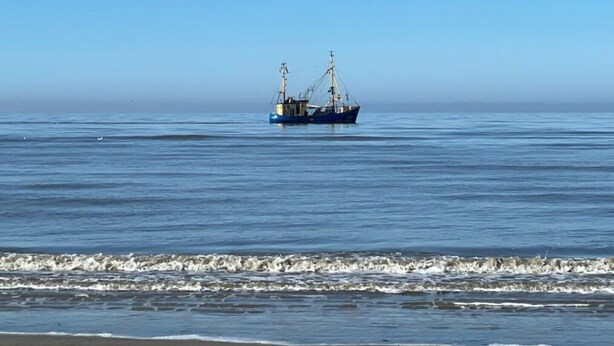 A fishing boat on calm waters near a beach.