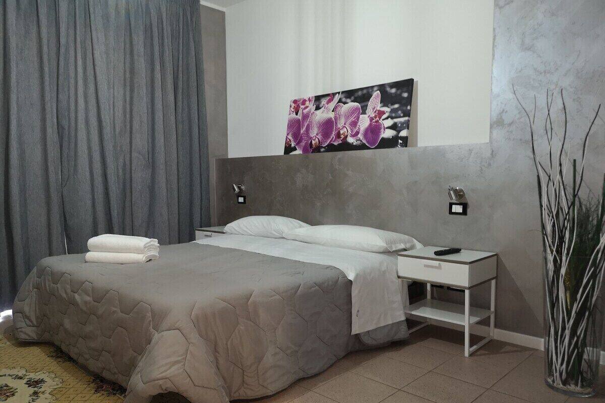 A modern bedroom with a large bed, a bedside table, a nightstand, a wall-mounted light, and a decorative wall piece.