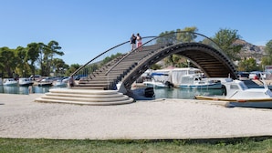 Un pont piétonnier doté d’une rambarde métallique, qui mène à une zone de quai où sont amarrés des bateaux.