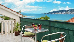 Un balcon avec une table et des chaises, offrant une vue sur la côte, avec un ciel dégagé et des bâtiments situés au loin.