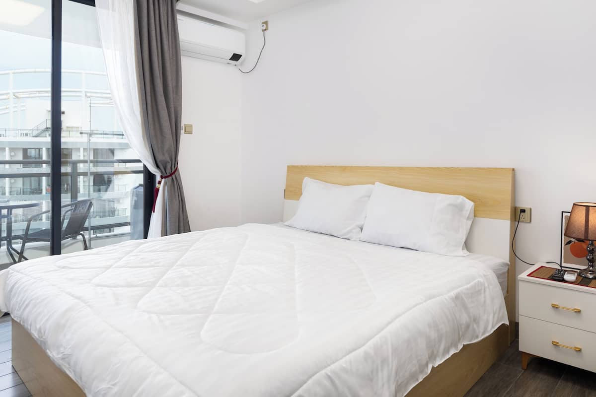 Ein Hotelzimmer mit einem großen Bett, einem Nachttisch mit Lampe und Blick auf einen Balkon mit Gartenmöbeln.