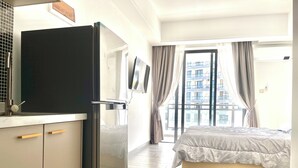 A hotel room with a bed, a TV mounted on the wall, a refrigerator, and a window with curtains. - Star Bay Residence (Sihanoukville)