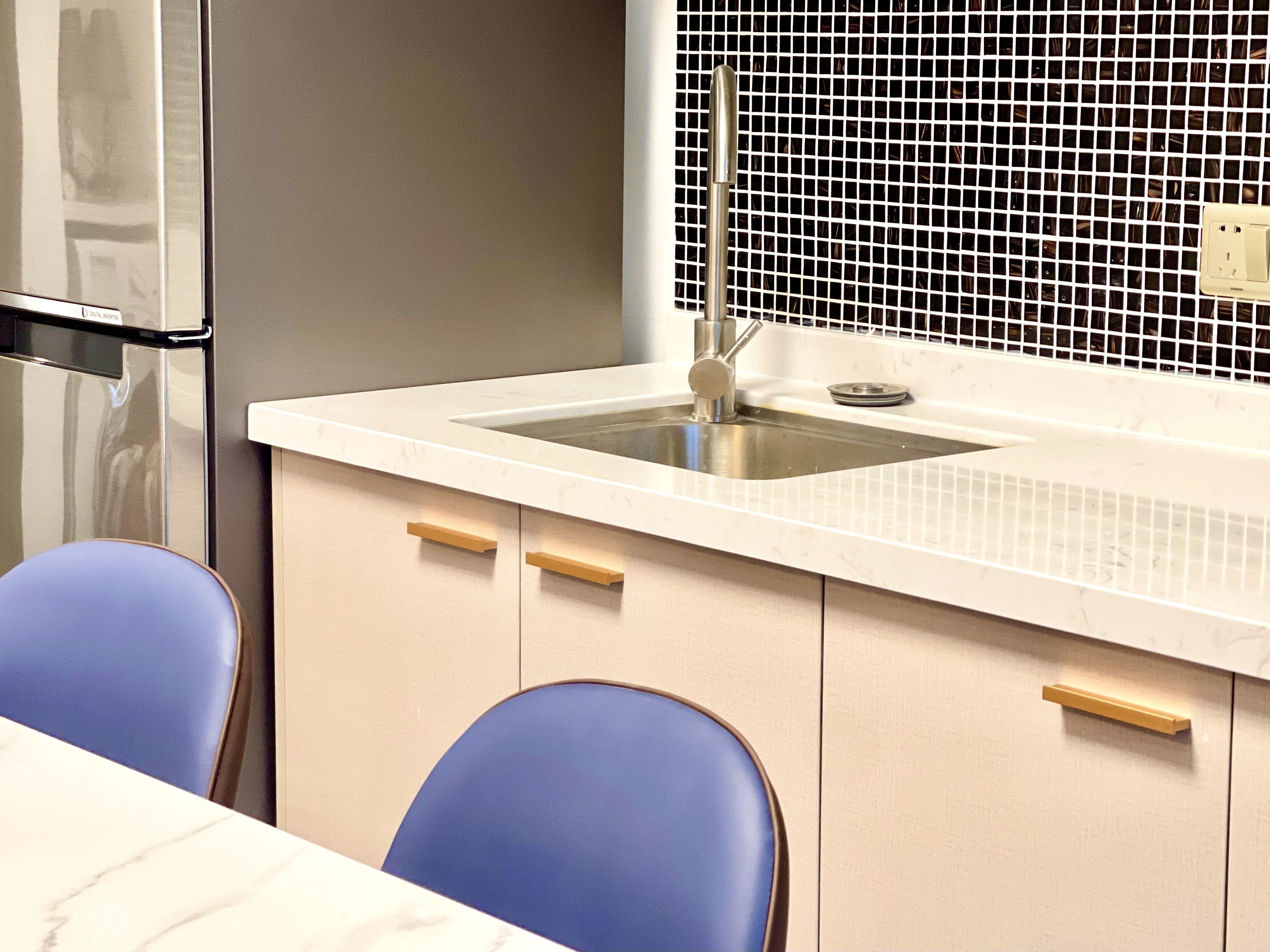 A modern kitchen with a stainless steel sink, white countertop, and beige cabinets.