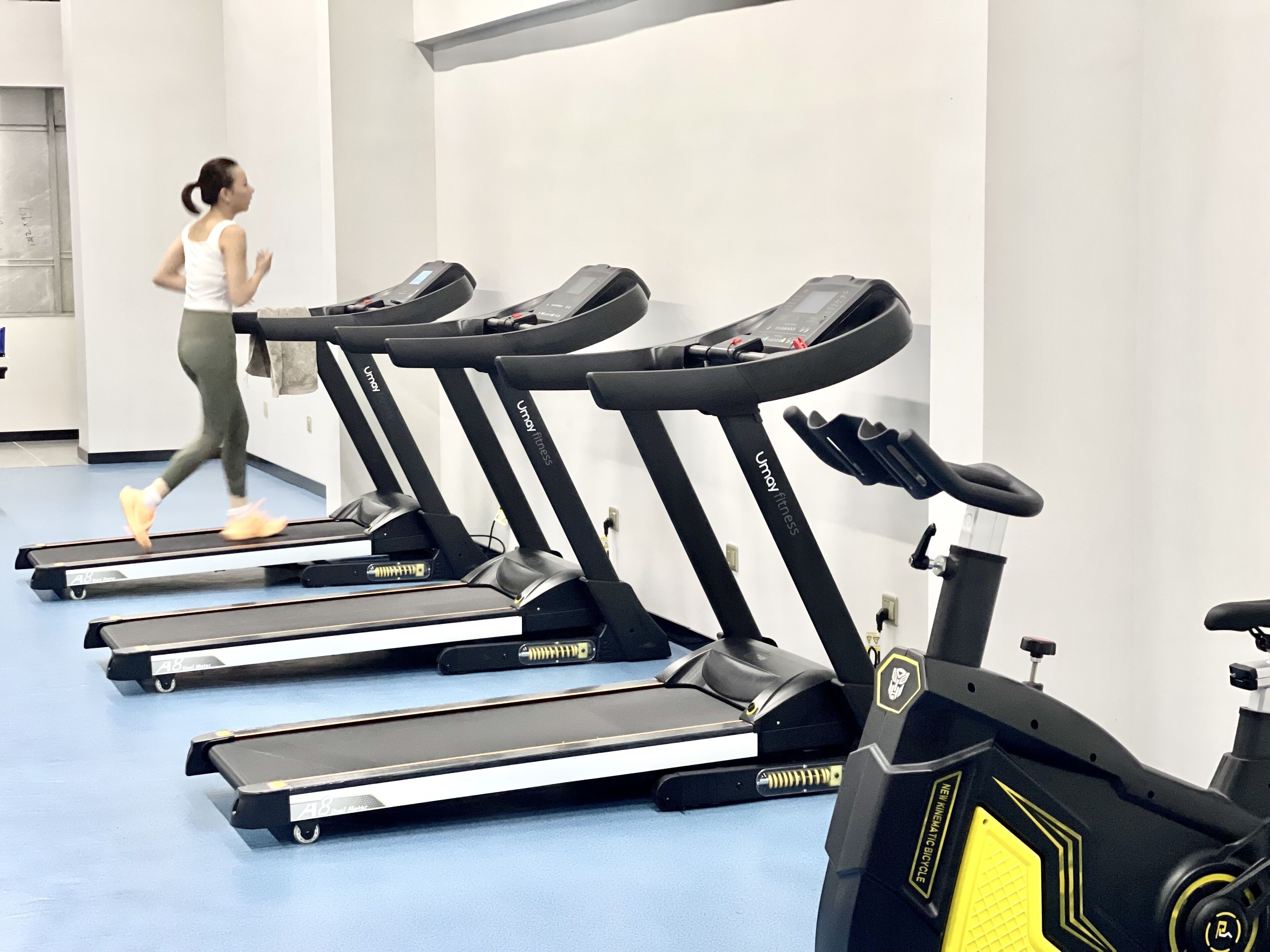 Une rangée de tapis de course dans une salle de sport, avec une personne qui court sur l'un d'eux.