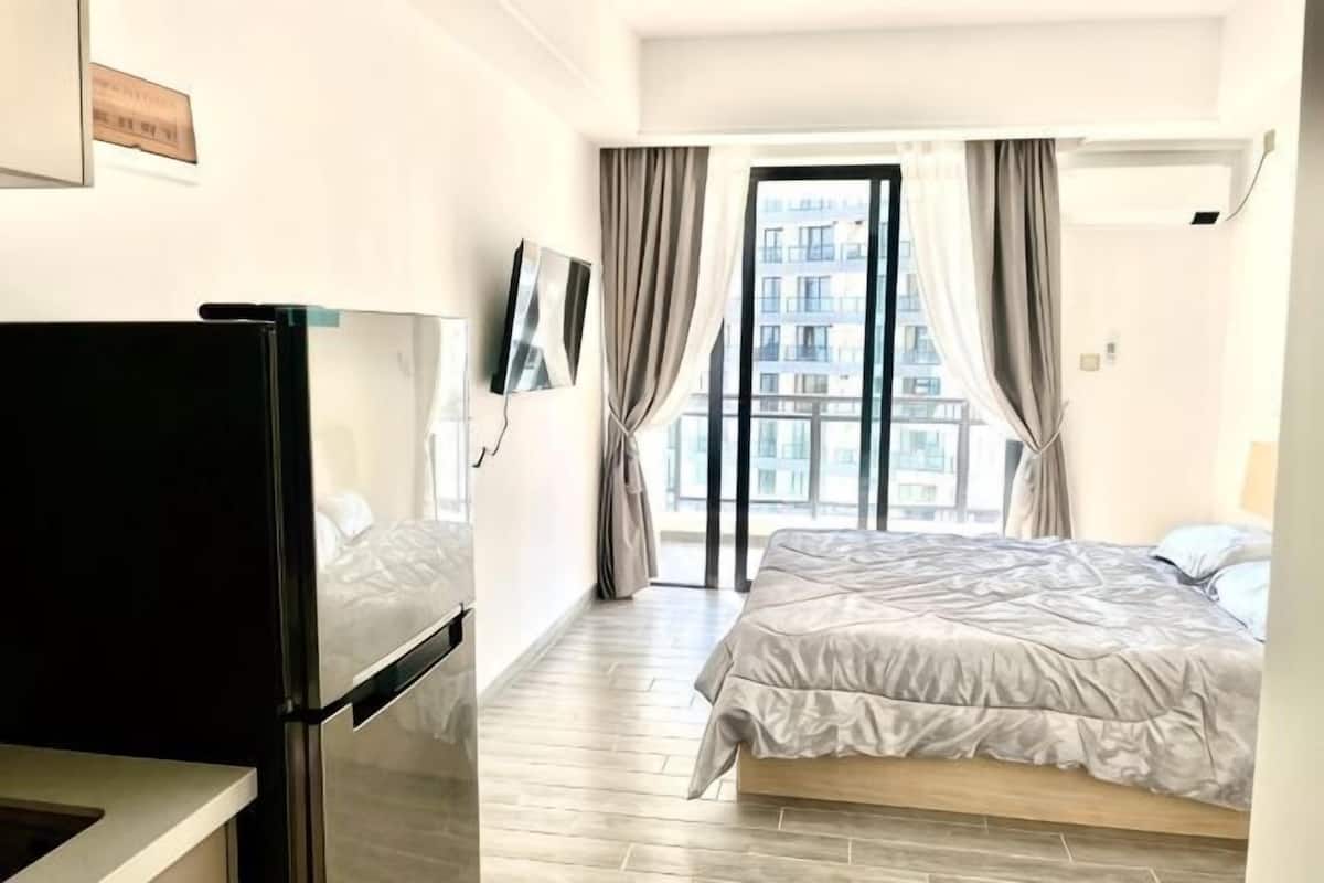 Ein Hotelzimmer mit Bett, Fernseher, Kühlschrank und einem großen Fenster mit Vorhängen.