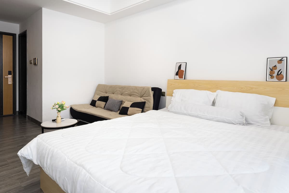 Ein Hotelzimmer mit einem großen Bett, einer Couch, einem kleinen runden Tisch mit Blumenvase und einem Holzkopfteil.