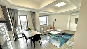 A modern living room with a dining area, a sofa, a coffee table, and a view of the city through large windows. - Star Bay Residence (Sihanoukville)