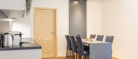 Cocina compacta con electrodomésticos modernos, zona de comedor con mesa y sillas, y una puerta de madera.