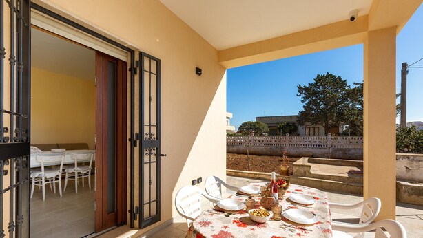 A balcony with a table set for dining, a sliding glass door leading to an indoor dining area, and a view of the surrounding area. - 3294 Villa Dolce Grazia by Barbarhouse (Manduria)