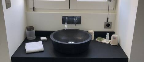 A bathroom with a black sink, two towel racks, a small basket, and a window with a view of trees.