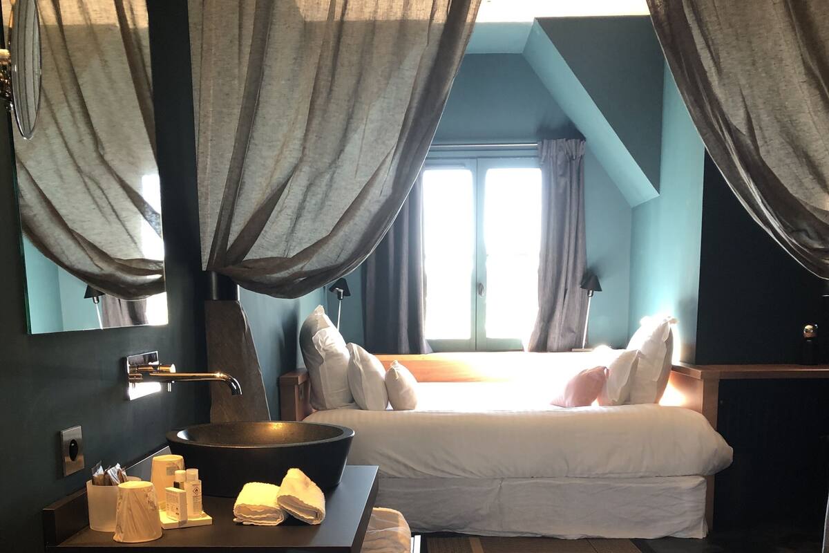 A modern hotel room with a large bed, a wooden desk, a sink, and a mirror.