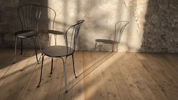 Una habitación con pared de piedra, suelo de madera y tres sillas de metal.