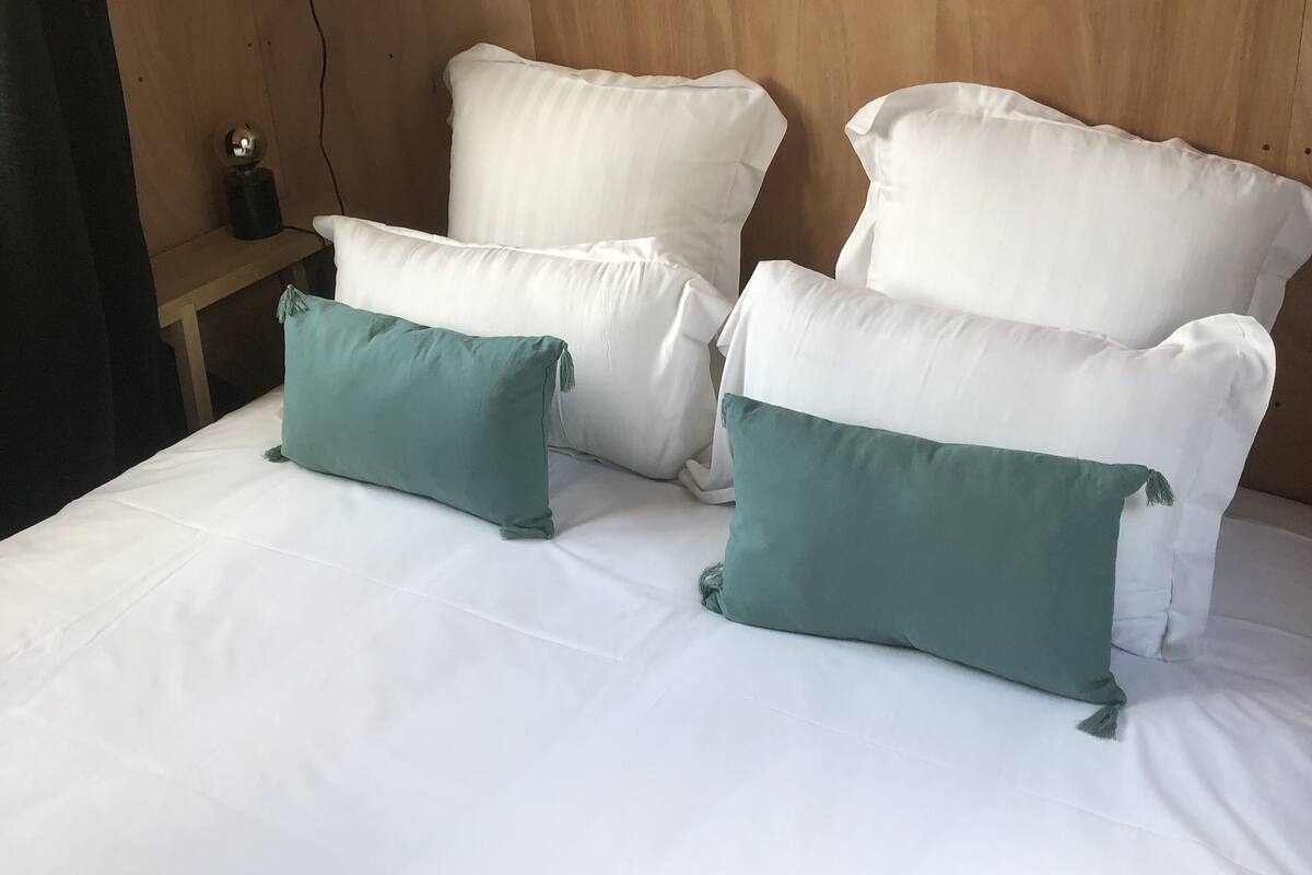A neatly made bed with white and teal pillows, a wooden headboard, and a small bedside table with a lamp.
