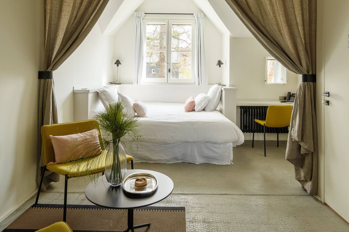 A bedroom with a bed, a chair, a table, and a window.