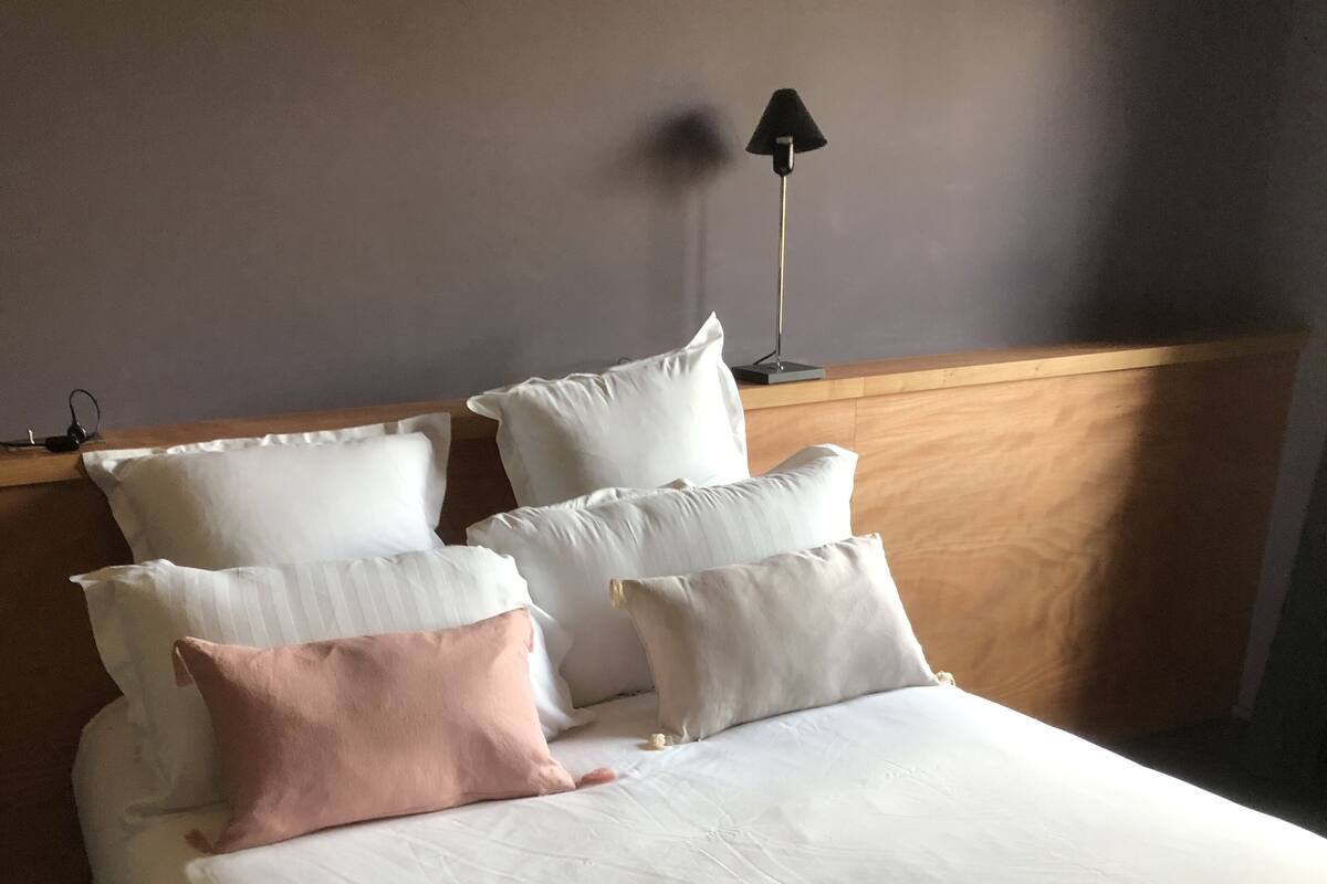 A neatly made bed with white and pink pillows, a wooden headboard, and a black floor lamp.