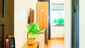 A hallway with a wooden bench, a potted plant, and a view of a garden through a window. - BAI CHAY PANDA HOTEL (Bai Chay)