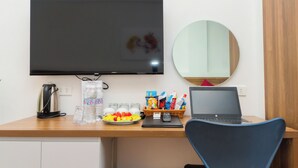 A hotel desk with a flat-screen TV, a laptop, a kettle, a basket of snacks, and a water bottle. - BAI CHAY PANDA HOTEL (Bai Chay)