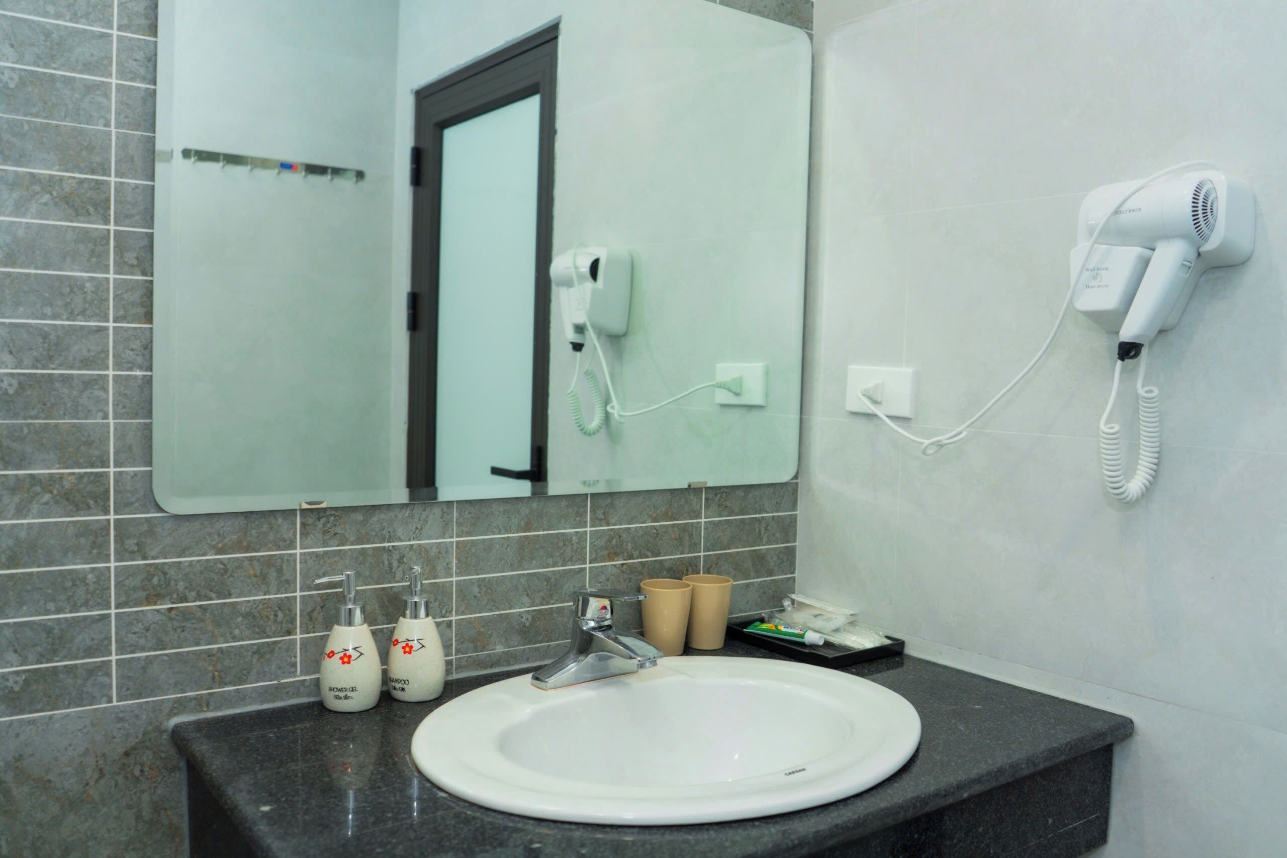 A bathroom with a sink, mirror, hairdryer, and toiletries.