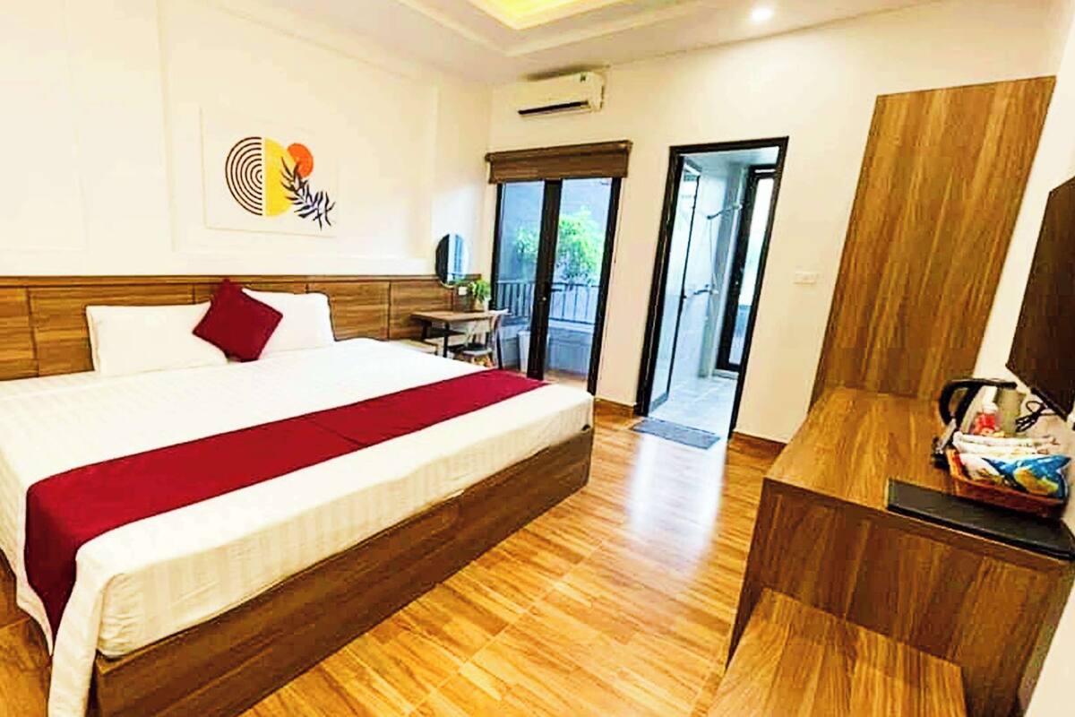 A hotel room with a large bed, wooden flooring, a desk, and a view of the outdoors.